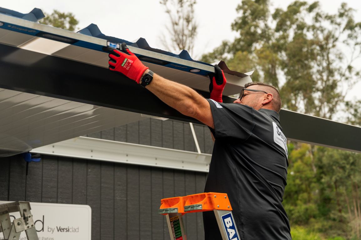 Person installing a roof gutter system with a ladder and tools.