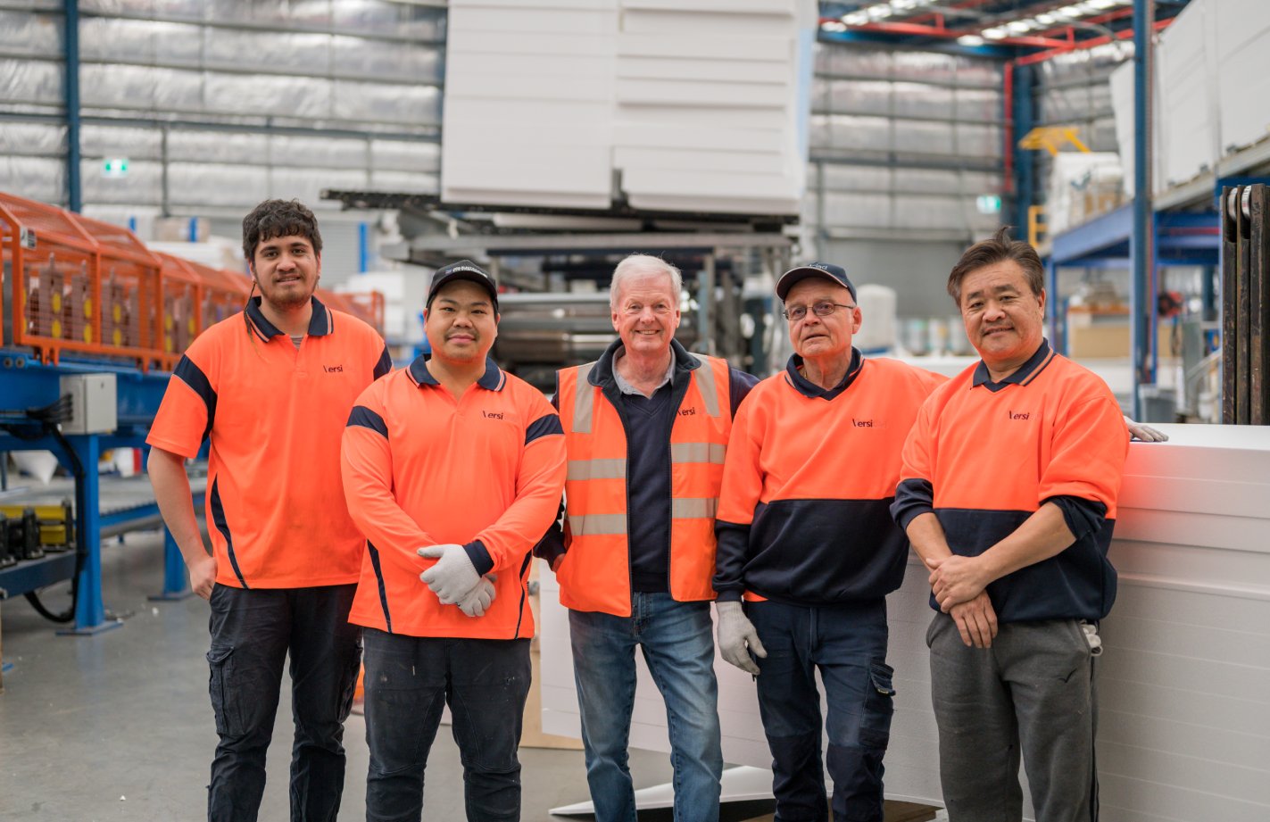 Group of people in a warehouse setting, wearing safety vests and uniforms.