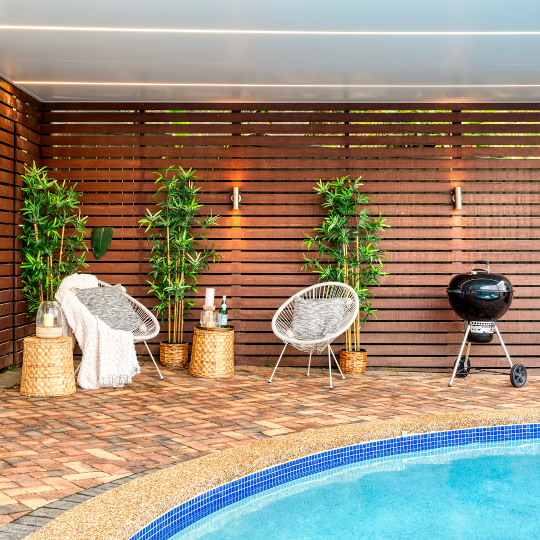 Outdoor patio area with chairs, plants, and a barbecue next to a pool.